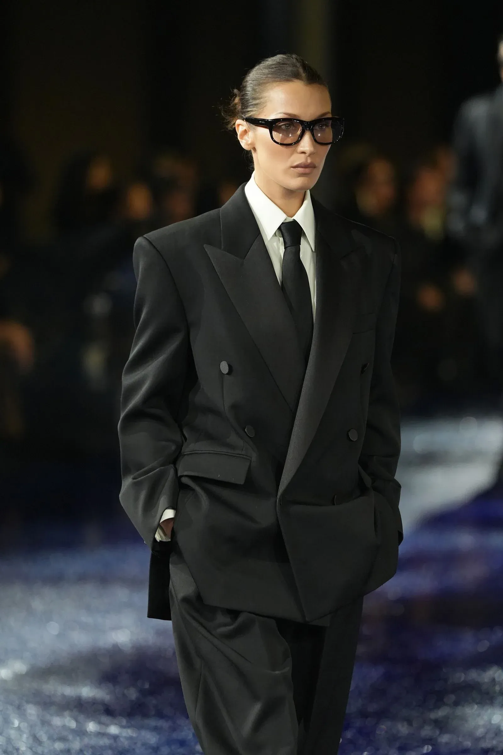 Mannequin en costume noir et lunettes de vue noires sur un podium de défilé