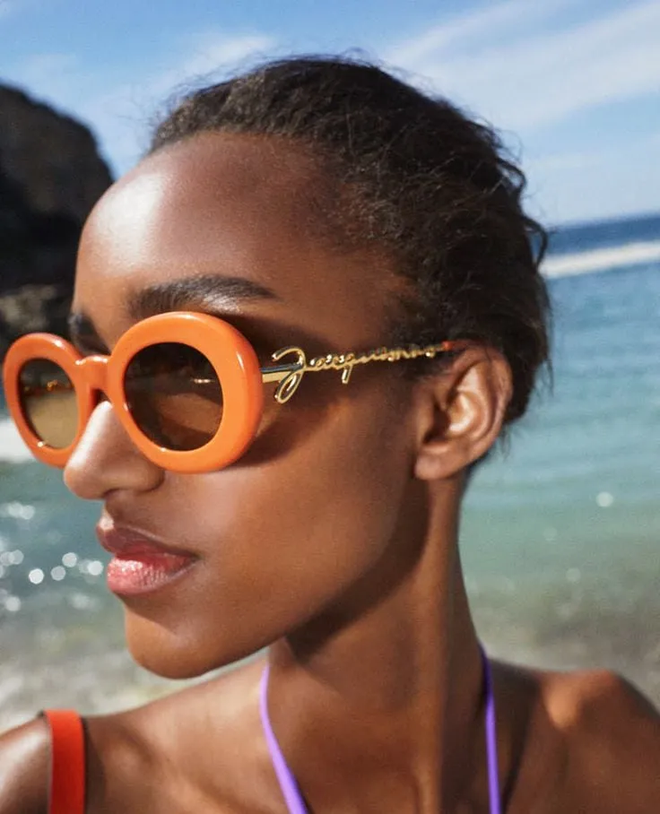 Femme portant des solaires Jacquemus ovales orange, en bord de mer