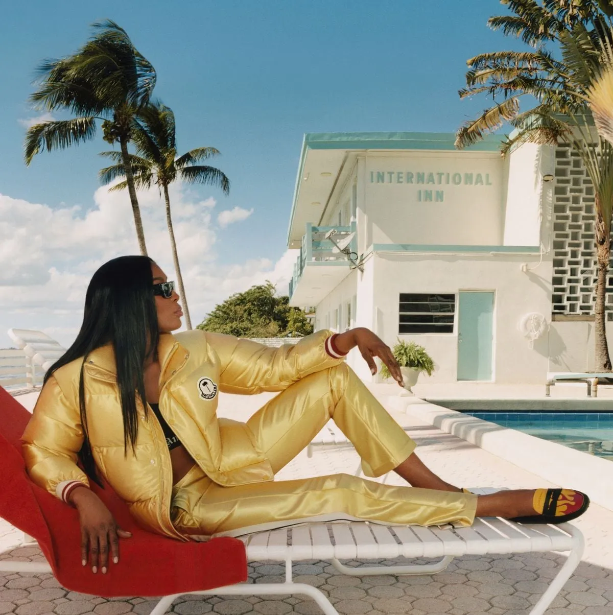Femme en lunettes de soleil allongée au bord d'une piscine, devant un motel