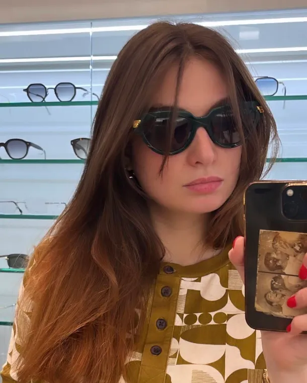 Cliente portant des lunettes de soleil vertes devant une vitrine de montures